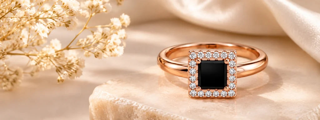 Rose gold halo ring with a dark square center, photographed on warm stone beside delicate flowers