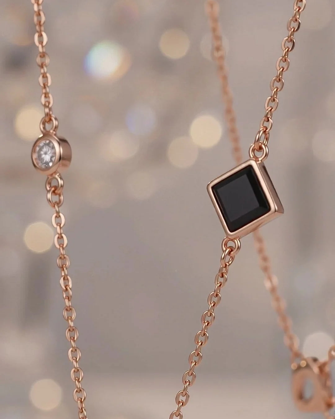 Close-up of a tiny dark square inset in a rose gold chain, with soft warm lights behind it